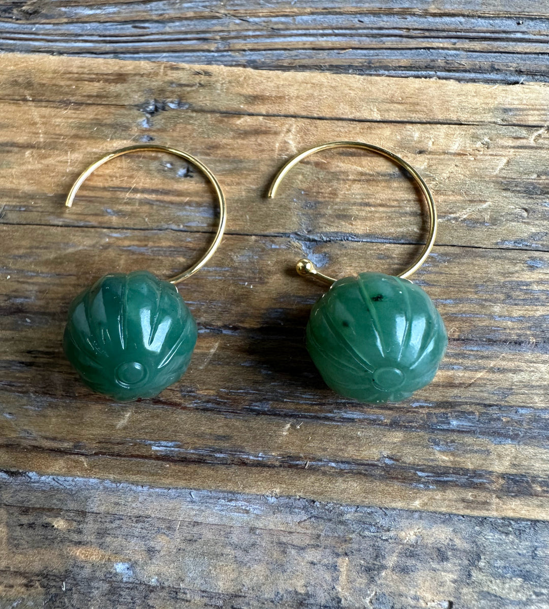 Pair of green jade drop bead earrings 13mm with gold hoops resting on a wooden surface.