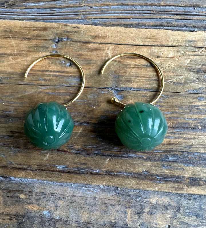 Pair of green jade drop bead earrings 13mm with gold hoops resting on a wooden surface.
