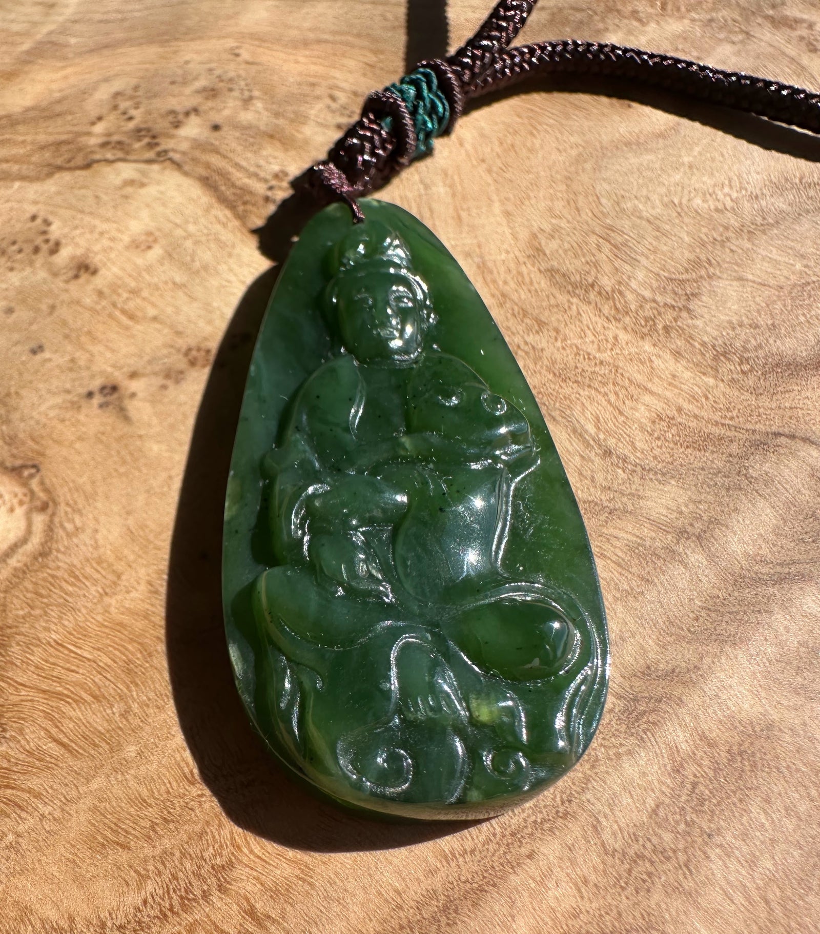 Green jade pendant with intricate carvings on a wooden surface