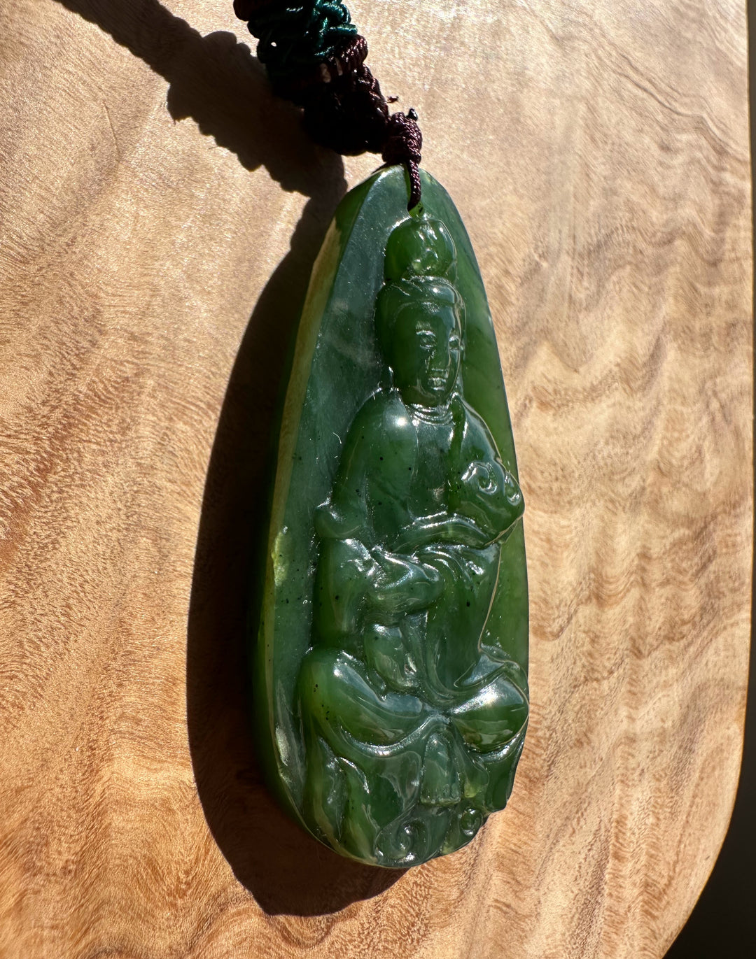 Green jade pendant with a figure on a wooden surface