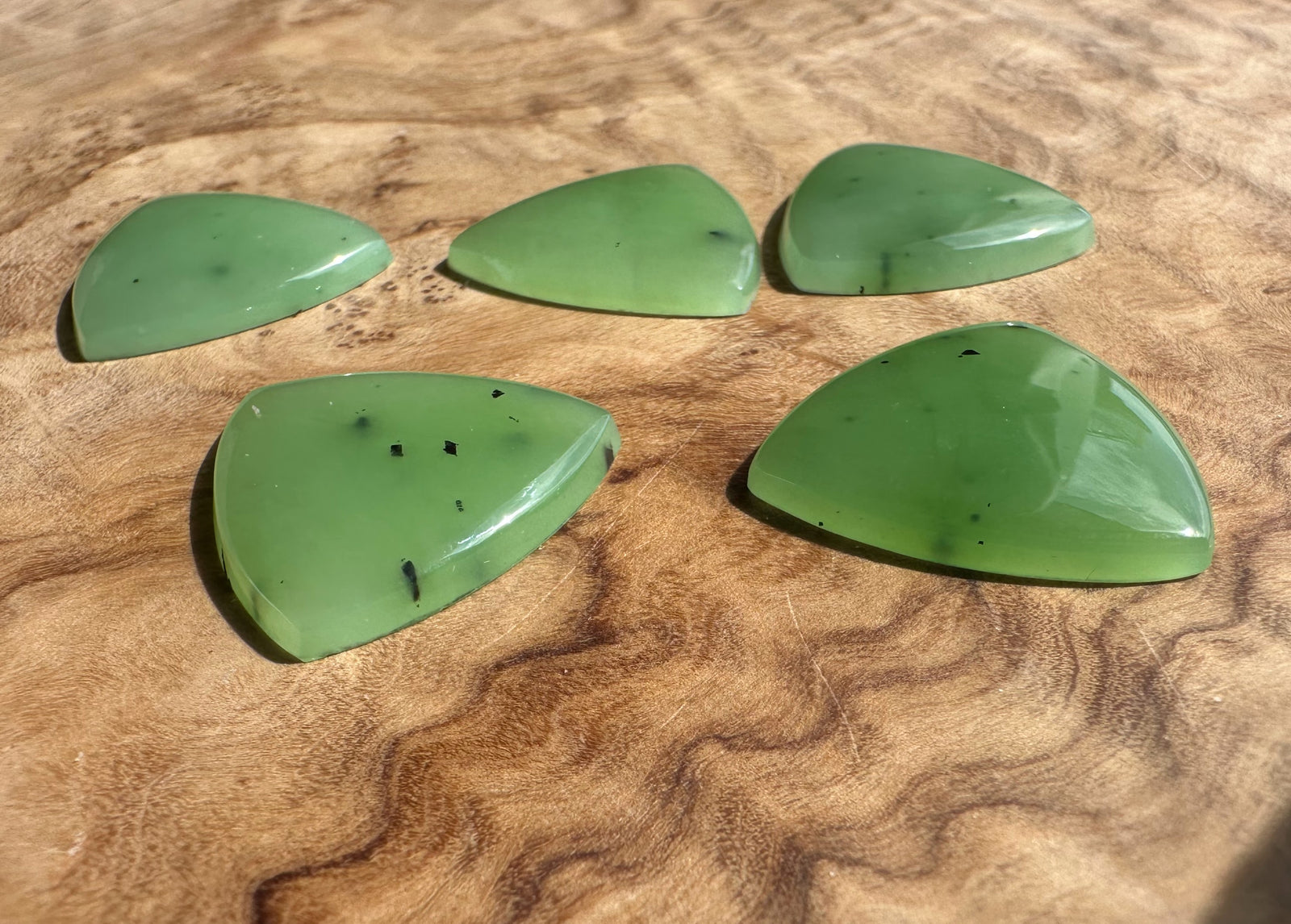 Five apple green Siberian jade cabochons in teardrop shapes on a wood surface