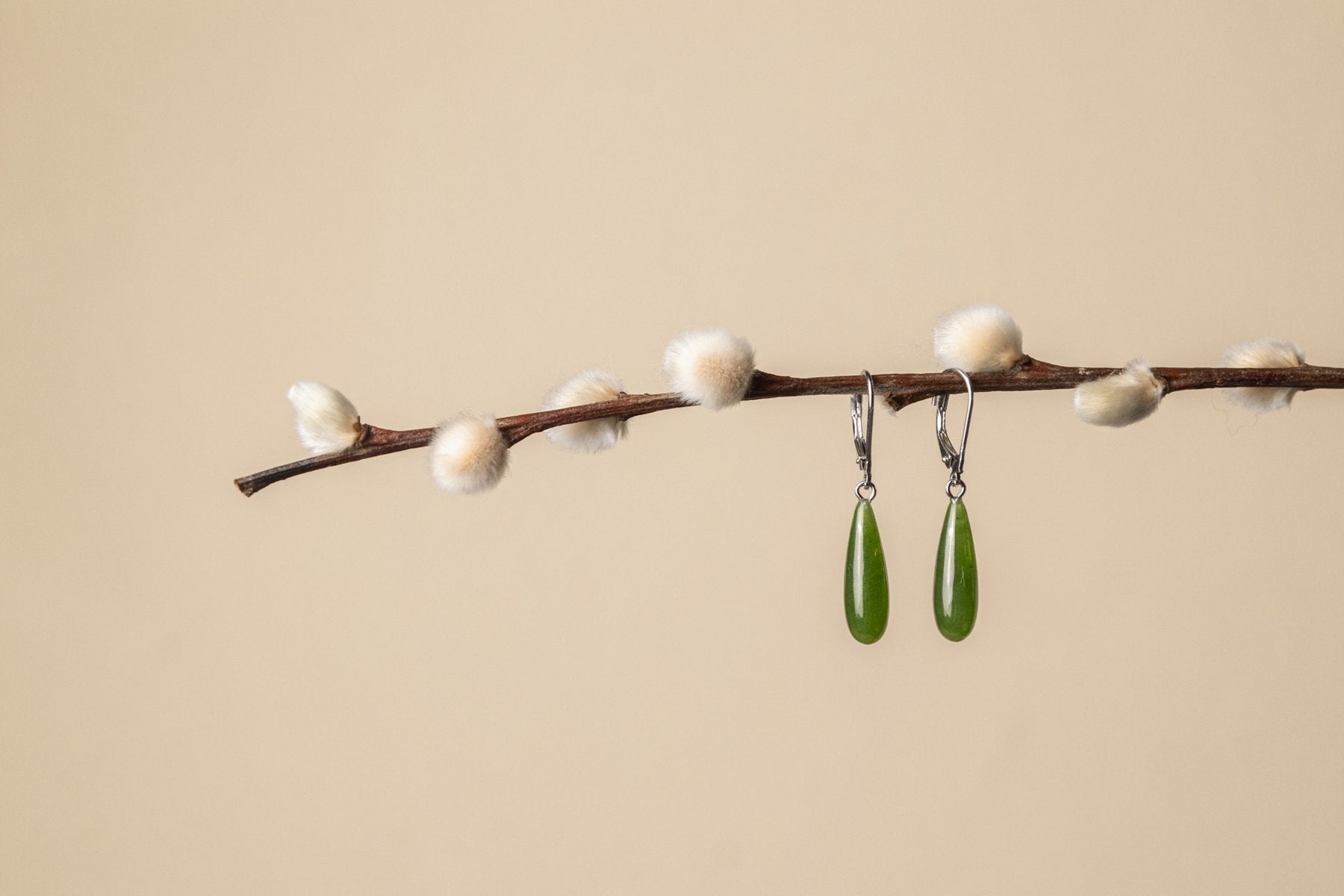Canadian Jade Earrings, hanging on a pussy willow branch with a beige background 