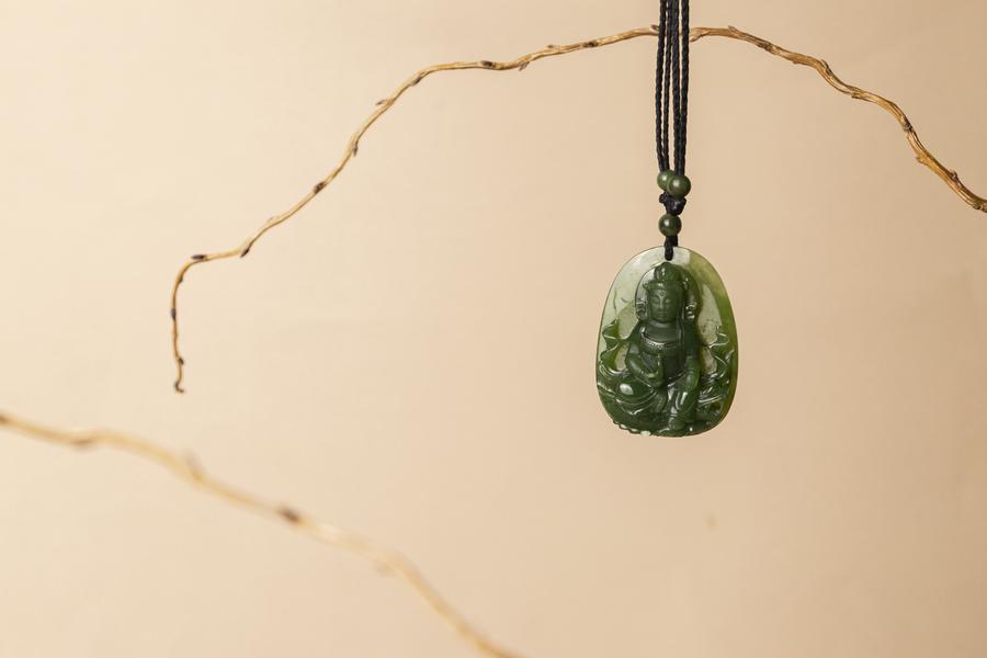 Green Jade Guanyin Buddha on a black cord, with a beige background and sticks