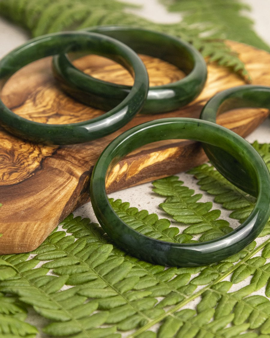 4 Canadian Jade Green Bangles laying on top of fern and a woode base 