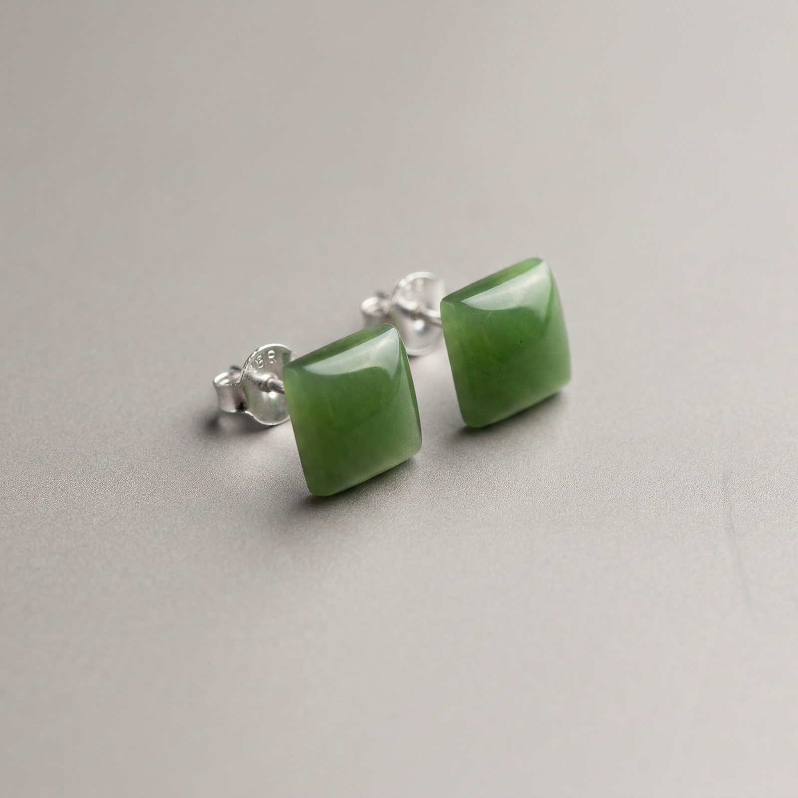 Green jade square stud earrings with silver posts on a neutral gray background.