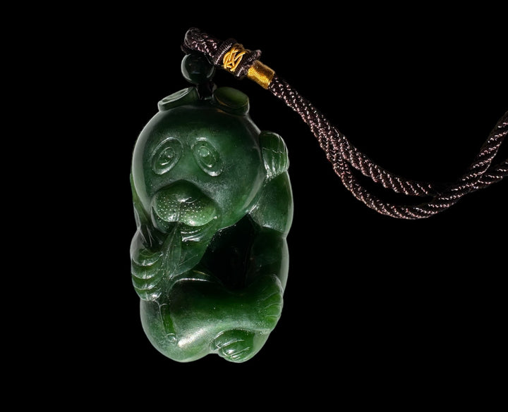 Dark green jade panda pocket pendant suspended by a braided black cord with gold wrap against black background