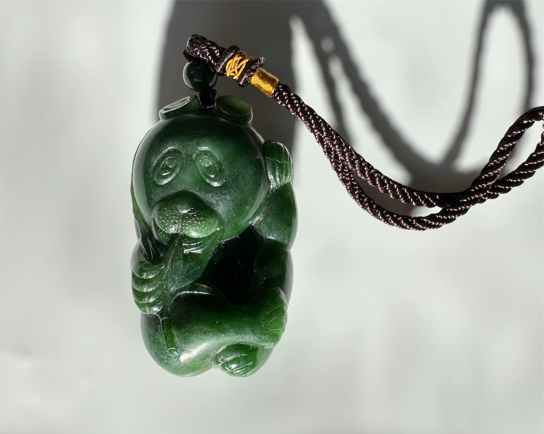 Panda jade pendant on a dark braided cord against a pale background.