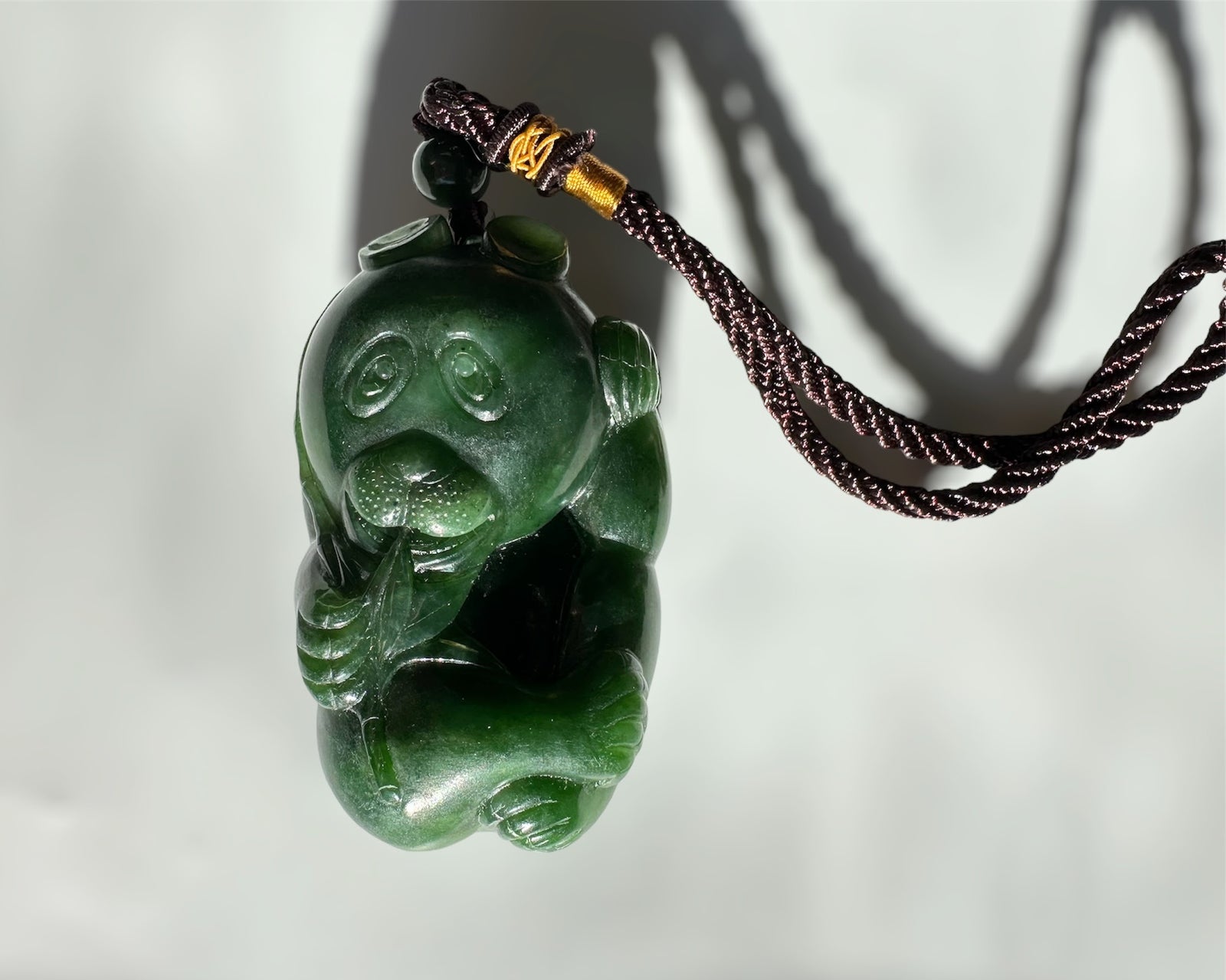 Panda jade pendant on a dark braided cord against a pale background.