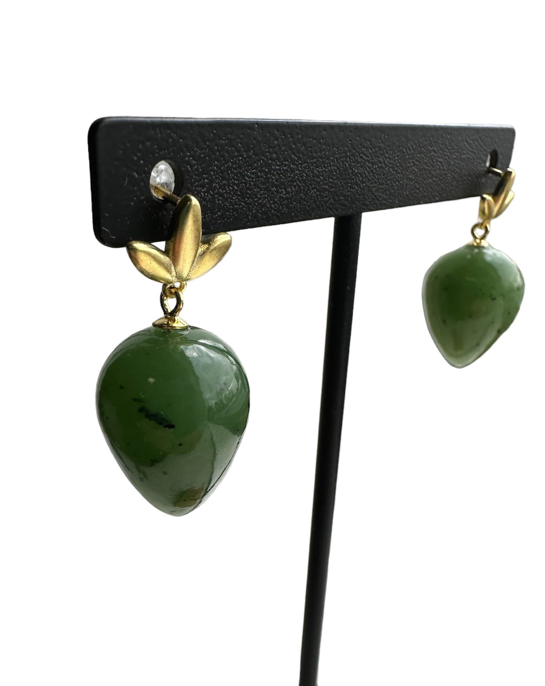 Gold leaf accent earrings with large green jade heart drops on a black display stand