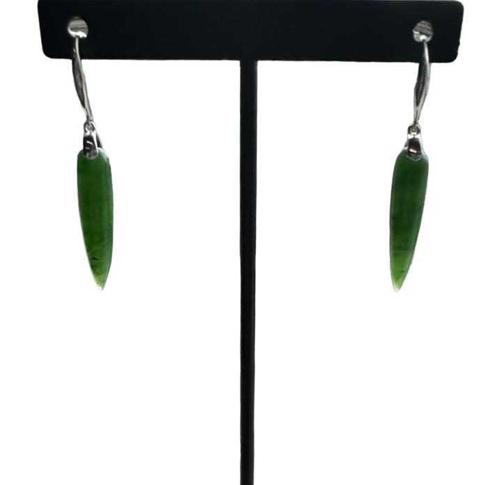 Two green jade drop earrings with silver hooks displayed on a black stand.