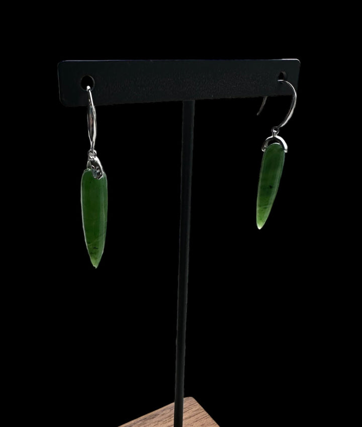 Green jade drop earrings with silver hooks hanging from a black display stand.