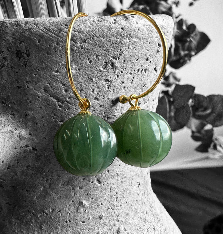 Green jade drop bead earrings 13mm with gold hoops photographed on a textured stone background.