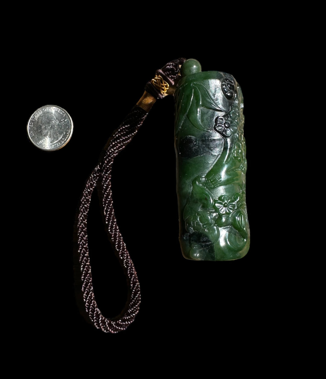Green jade carved pendant with floral details and a braided brown cord for scale against a black background