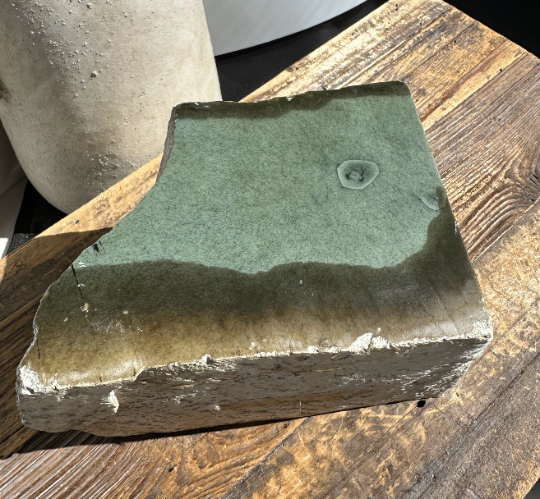 Wyoming Sage rock slab with olive green surface and pale rough edge on a wooden table