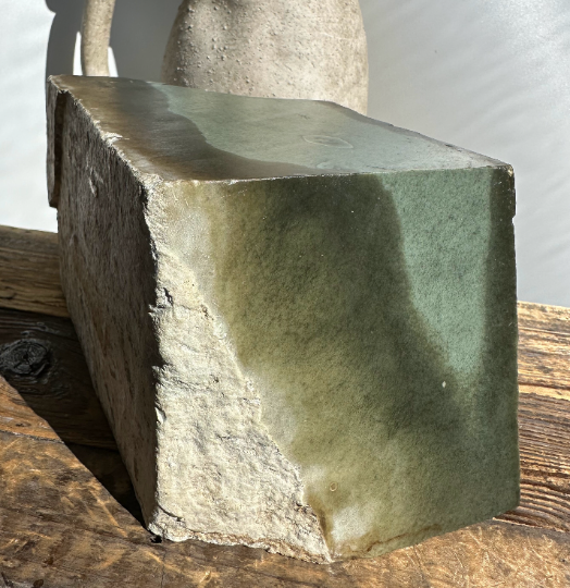 Wyoming Sage mineral block with green glaze and white crust on a wooden surface.