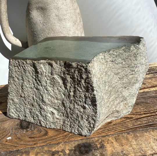 Wyoming Sage mineral block viewed from the side with a green top and coarse gray exterior on a wooden table.