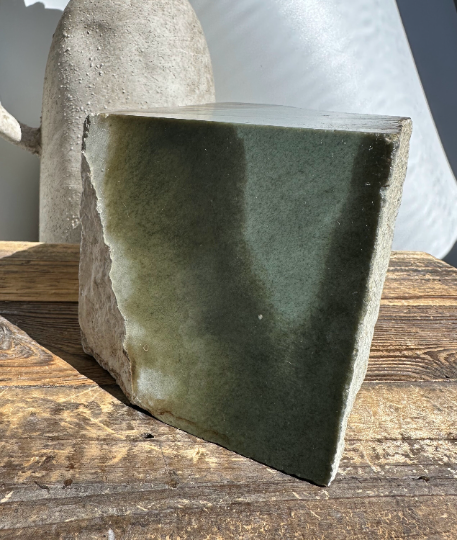 Wyoming Sage mineral slab with a green face and rugged gray edges on a wooden surface.