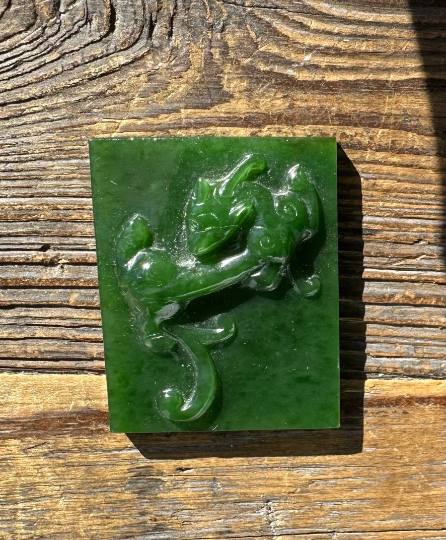Green A+ Siberian nephrite jade plaque with a dragon relief resting on a wooden surface.