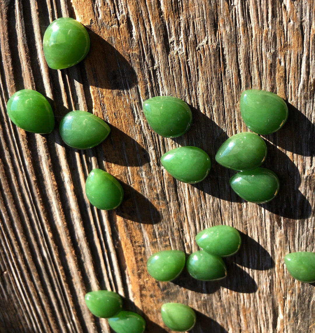 Group of bright green pear shaped cabochons scattered on a rustic wooden surface