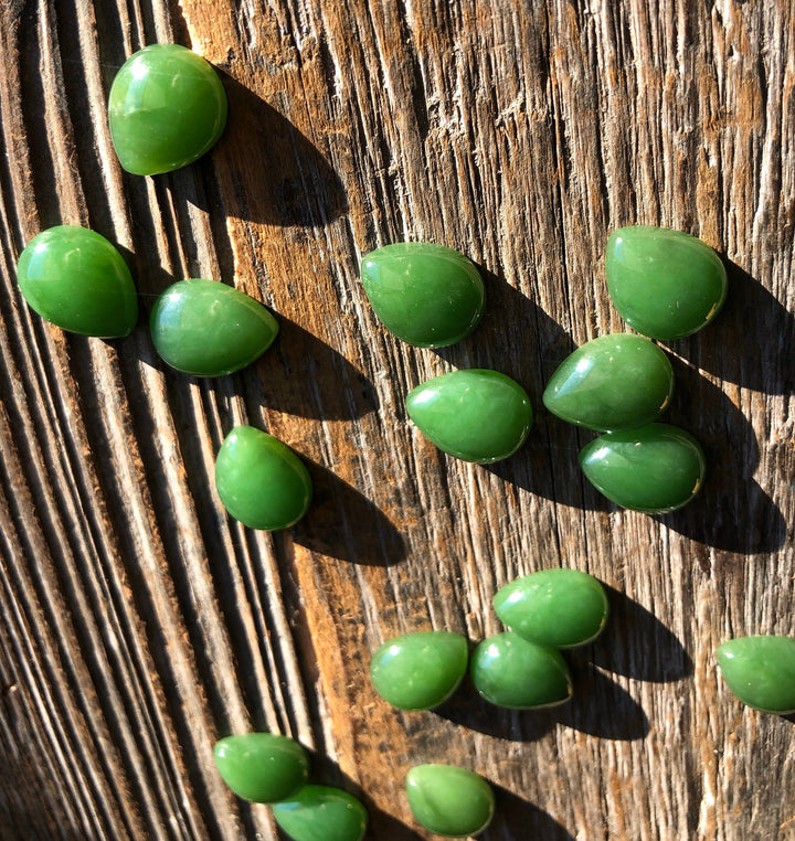 Group of bright green pear shaped cabochons scattered on a rustic wooden surface