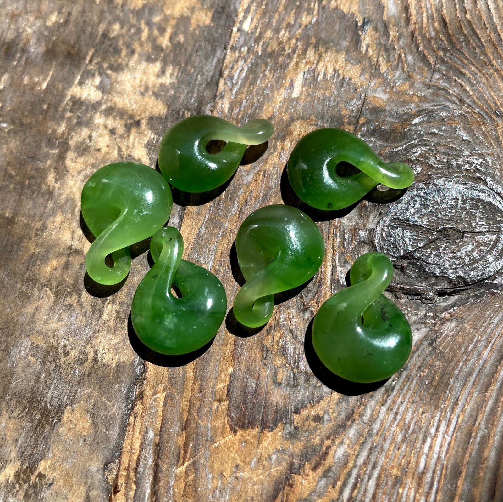 Group of green jade infinity twist pendants arranged on a textured wooden surface.