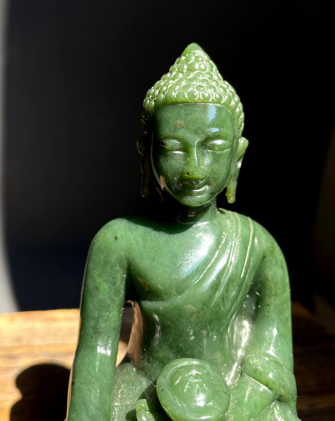 Close-up of a green jade Buddha head and shoulders against a dark background.