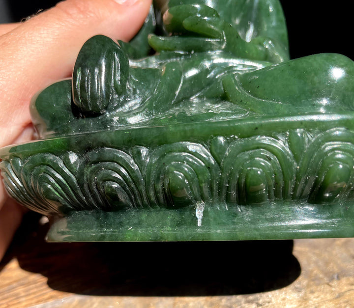 Close-up of the jade statue base with swirling carvings and a finger visible for scale.