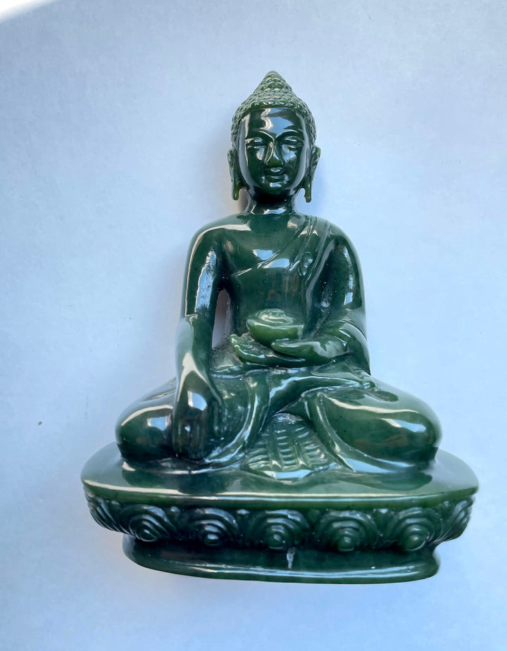 Front view of a dark green jade Buddha statue seated in meditation against a pale blue background.