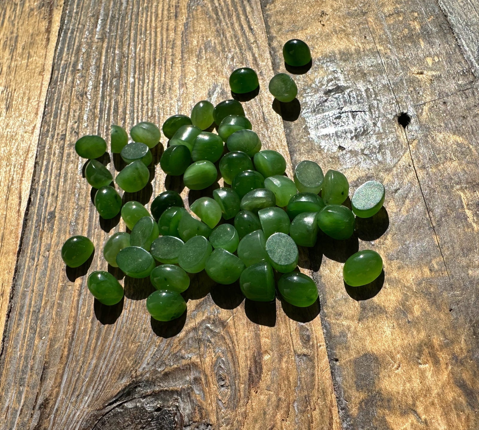 A grade green jade cabochons 8x6mm high dome scattered on a weathered wood surface