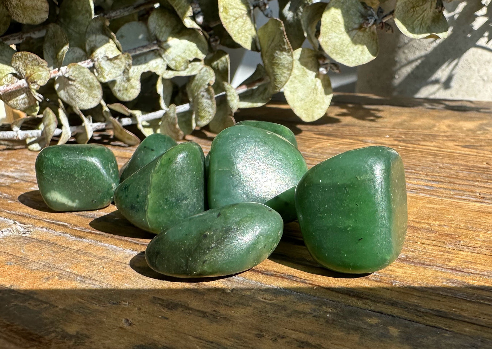 Group of satin green jade nuggets in various shapes resting on a wooden surface.