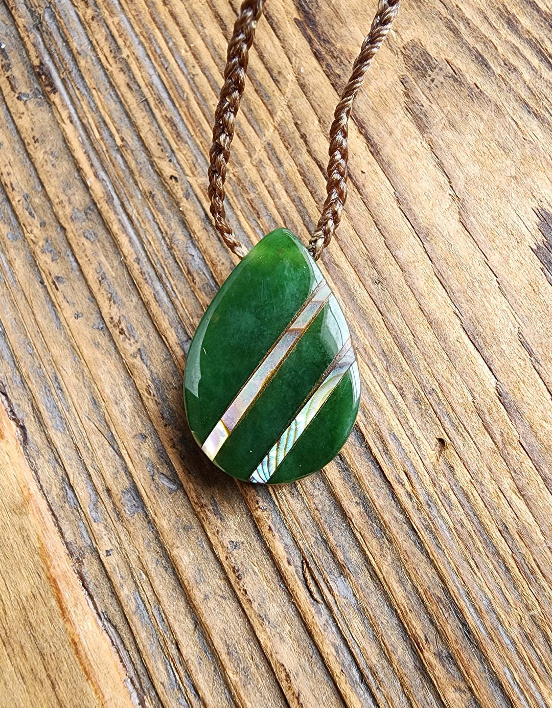 Green nephrite jade teardrop pendant with diagonal abalone inlay on a brown braided cord
