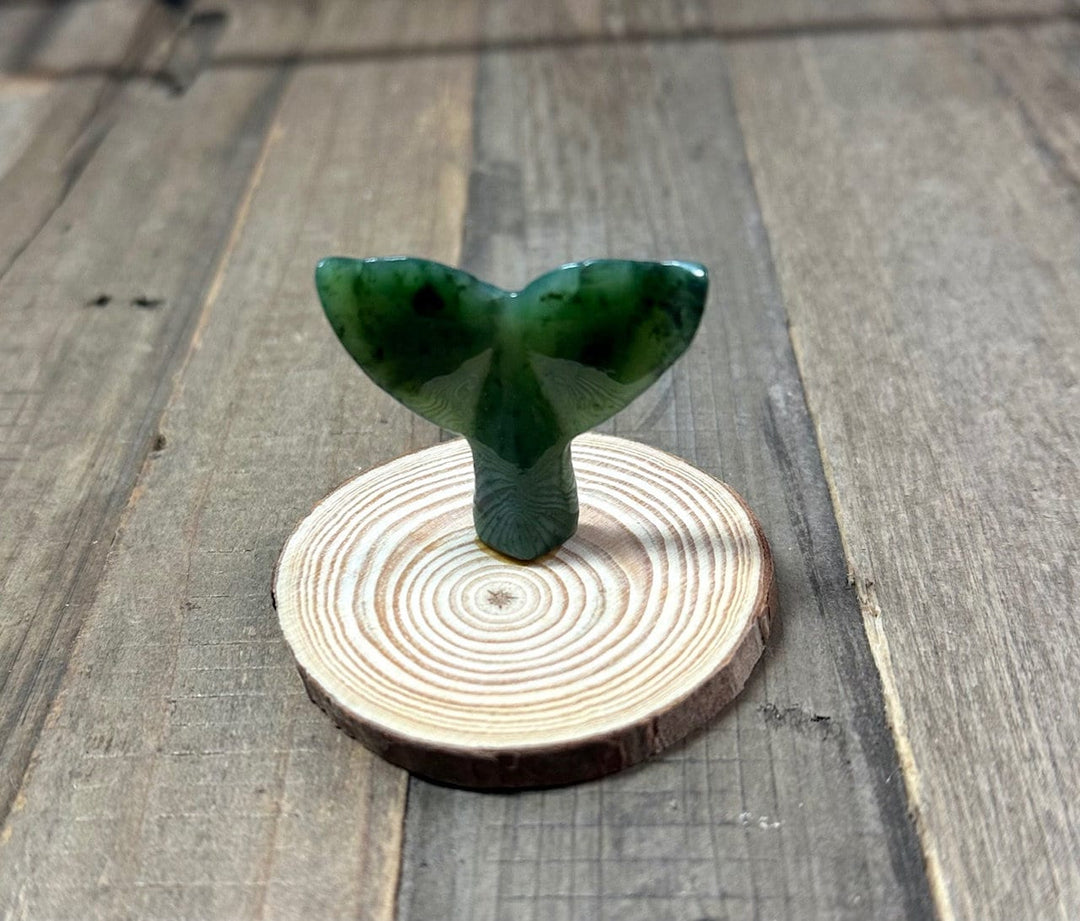 Close view of a green jade whale tail on a circular wood base.