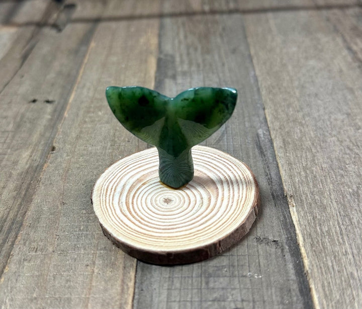 Close view of a green jade whale tail on a circular wood base.