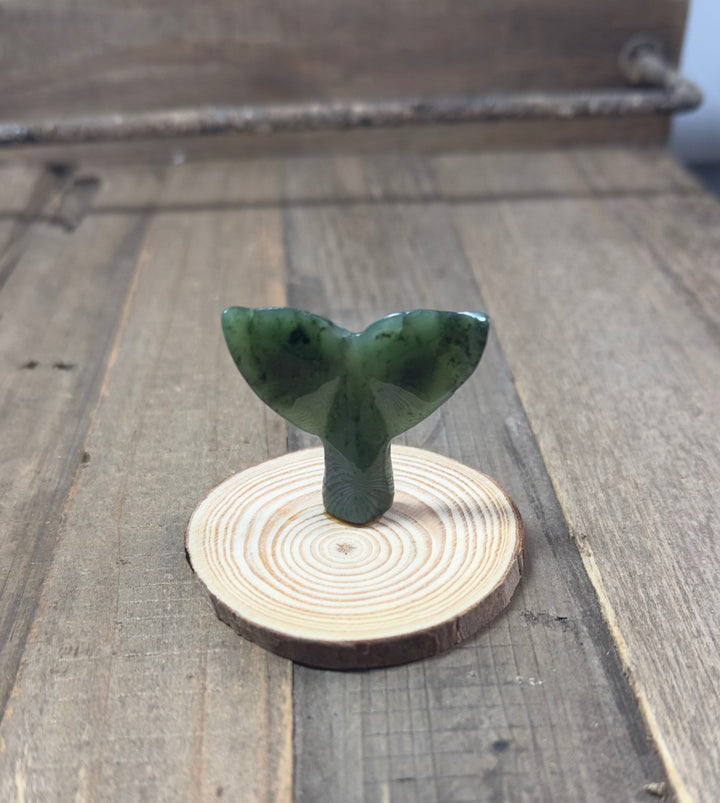 Green jade whale tail sculpture mounted on a circular wood base.