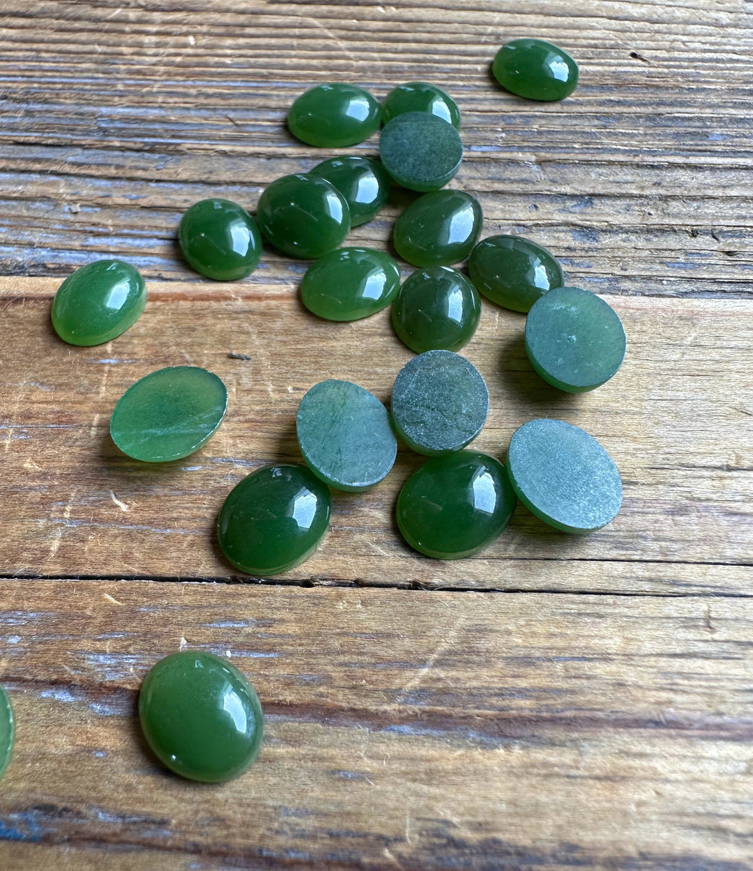 Glossy green 8x10mm Canadian Jade Oval Cabochons with some backs showing on wood