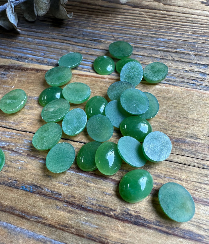 Back views of many 8x10mm Canadian Jade Oval Cabochons arranged on wood
