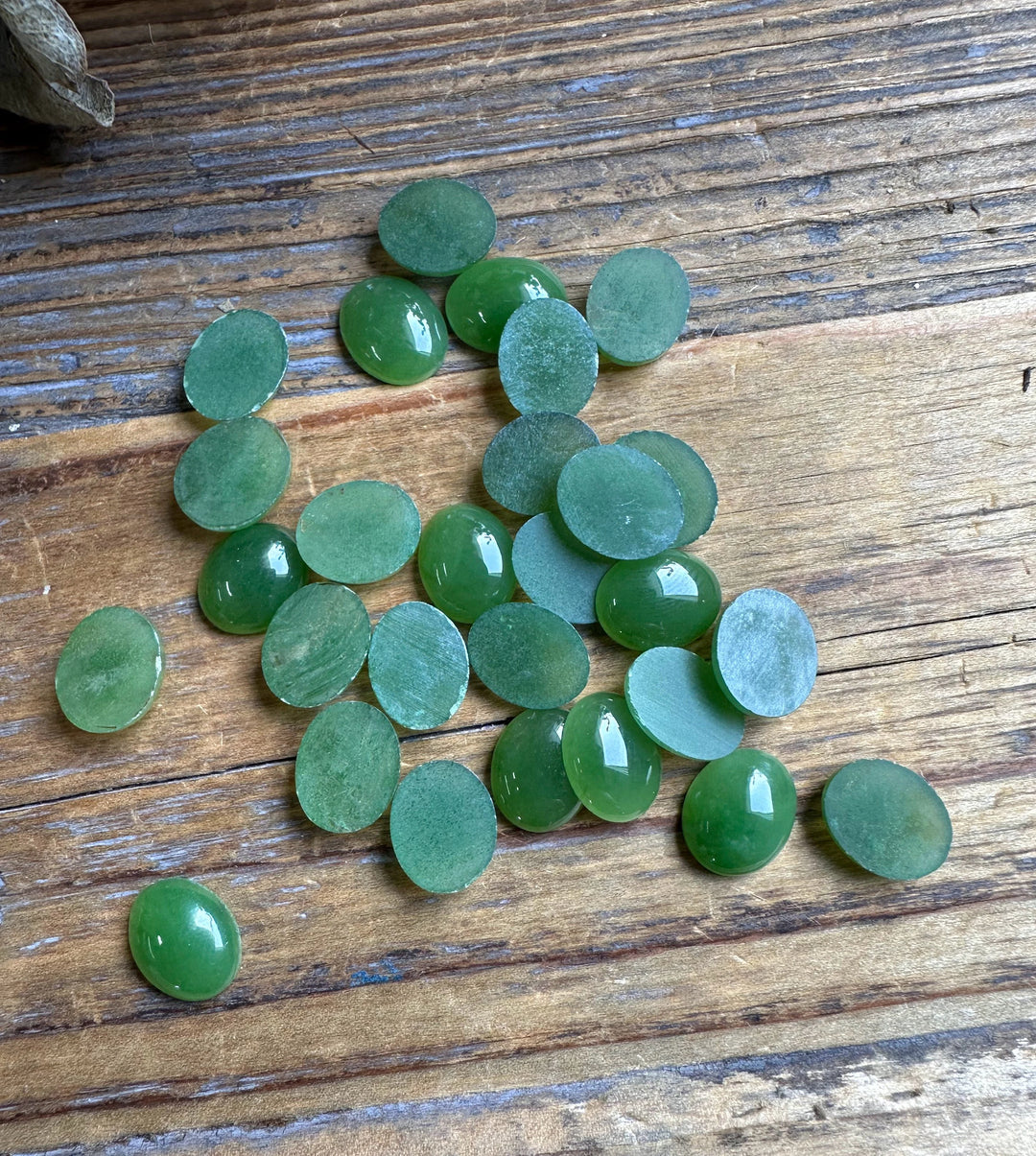 Green Canadian jade oval cabochons 8x10 mm scattered on a wooden surface