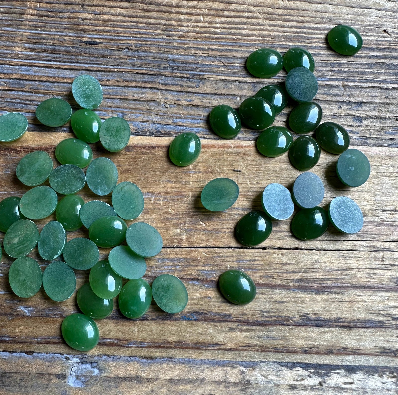 Group of green Canadian Jade Oval Cabochons 8x10mm scattered on rustic wood surface
