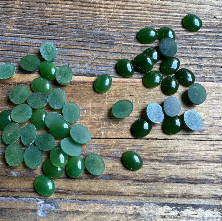 Group of green Canadian Jade Oval Cabochons 8x10mm scattered on rustic wood surface