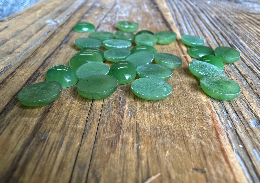 Flat-backed green Canadian jade oval cabochons 8x10 mm arranged on wood
