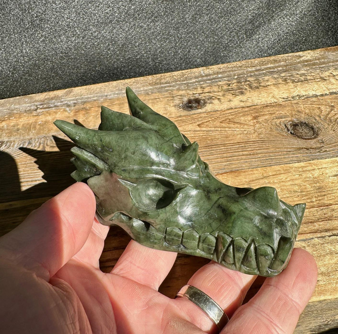 Jade dragon head sculpture in dark green stone side profile on a wooden surface in someone&