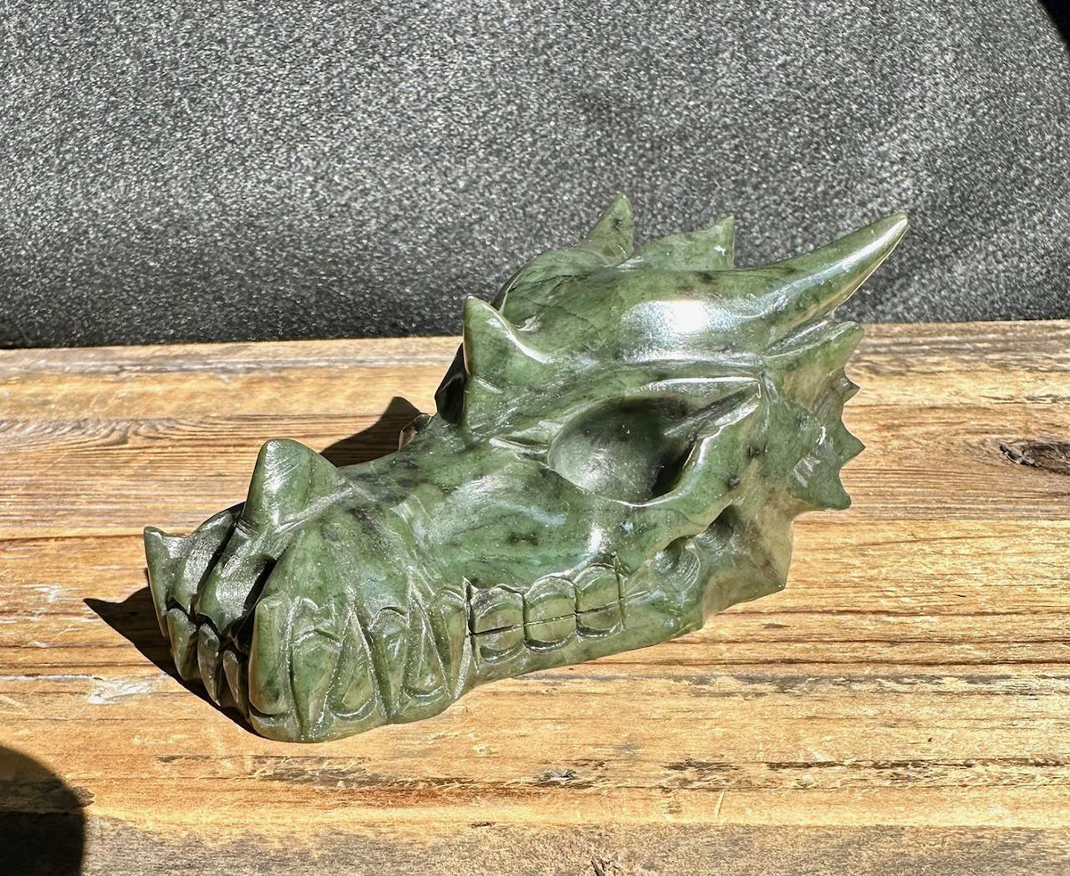 Jade dragon head sculpture in dark green stone side profile on a wooden surface
