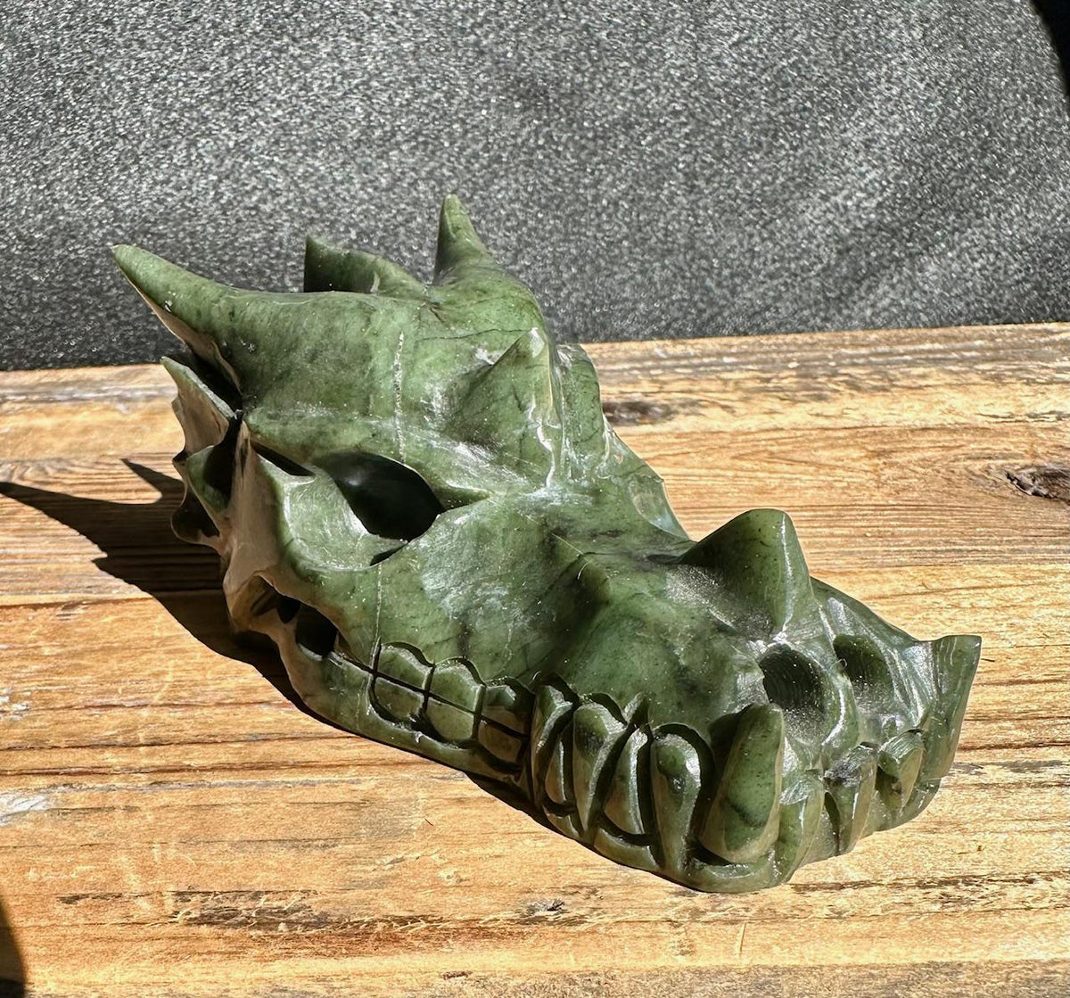 Jade dragon head sculpture in dark green stone side profile on a wooden surface