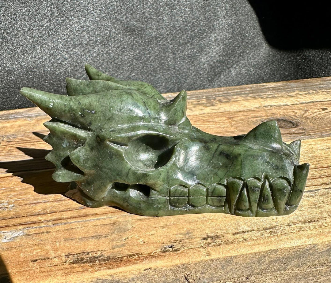 Jade dragon head sculpture in dark green stone side profile on a wooden surface
