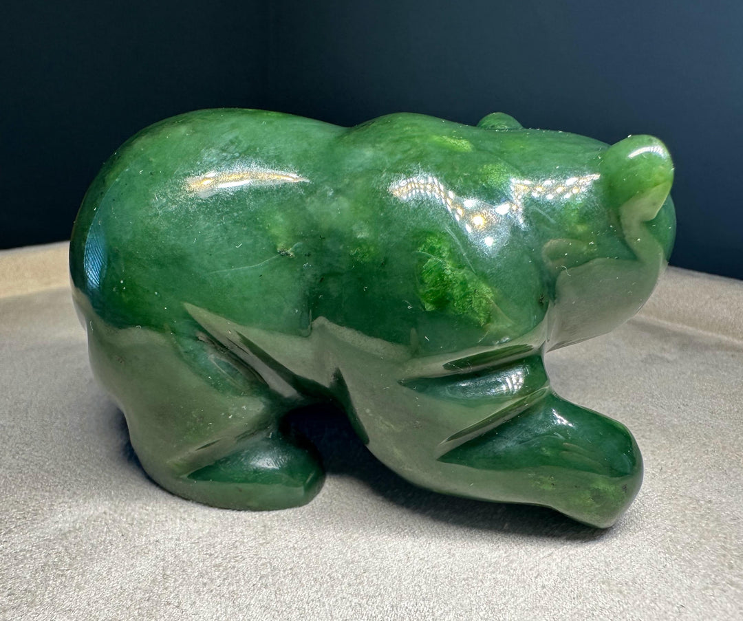 A polished green jade bear sculpture shown on a neutral fabric surface against a dark background.