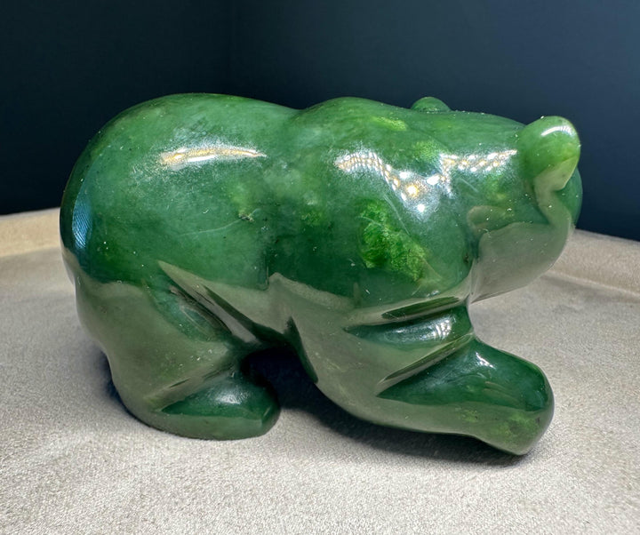 A polished green jade bear sculpture shown on a neutral fabric surface against a dark background.