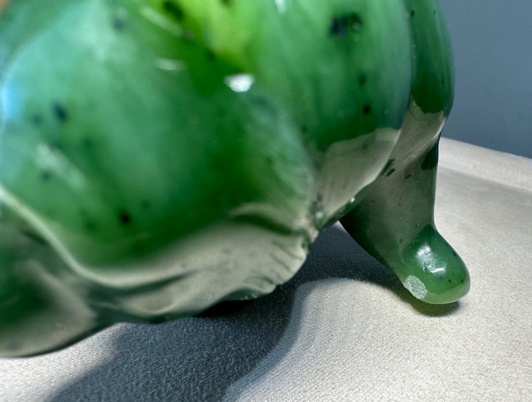 A close-up of the chips on a glossy green jade bear with dark speckles, resting on a light gray textured surface.