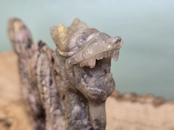 A close-up of a carved stone dragon head sculpture with an open mouth, showing detailed texture and pale gray-brown tones against a softly blurred background.