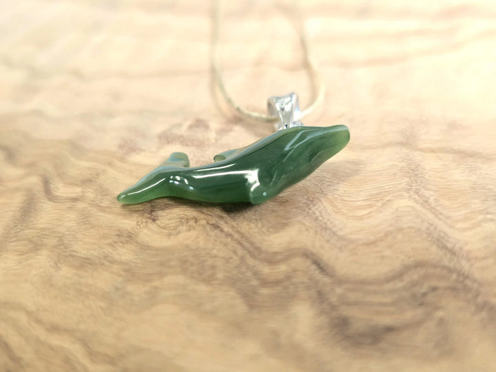 Green jade dolphin pendant with a silver bail lying on a wood grain surface