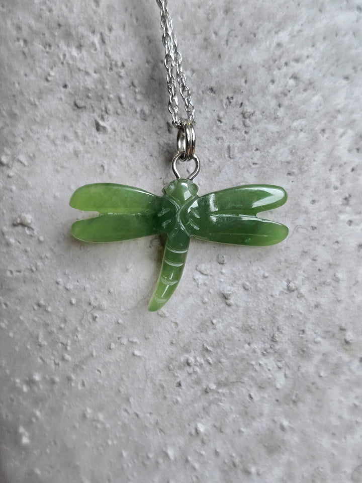 Green jade dragonfly pendant suspended from a chain against a textured light background